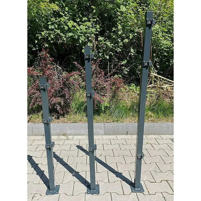 Peddy Shield Eckpfosten - Höhe: 130 cm, Anthrazit, Zum Einbetonieren - Drei graue Metallpfosten unterschiedlicher Höhe auf Pflastersteinen.
