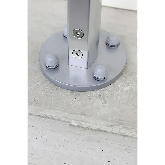 Tornillo autorroscante Blanco suelo de hormigón - 10 x 70 mm, Acero - Primer plano de un soporte de barandilla plateado con tornillos y pies redondos, situado sobre una superficie gris.