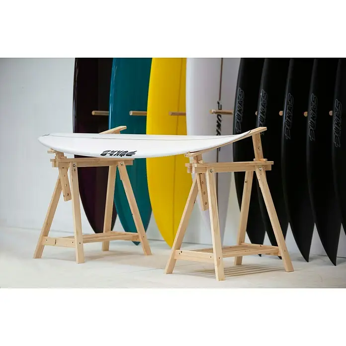 Astigarraga Holzbock Architekt - Tragkraft: 400 kg, Höhe: 70 cm, Kiefer, Natur - Surfbrett auf einem hölzernen Montageständer präsentiert, im Hintergrund eine Auswahl an farbigen Surfbrettern.