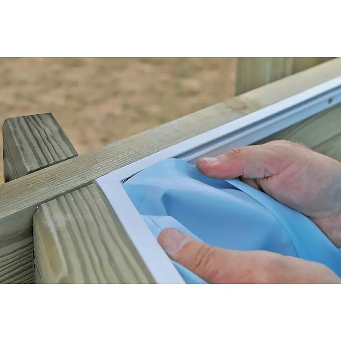 Gre Holz-Pool City - L x B x H: 225 x 225 x 68 cm, Braun, 2.300 l - Nahaufnahme von Händen, die ein blaues Werkzeug zur Montage von weißen Terrassendielenhaltern an einem Holzrahmen verwenden.
