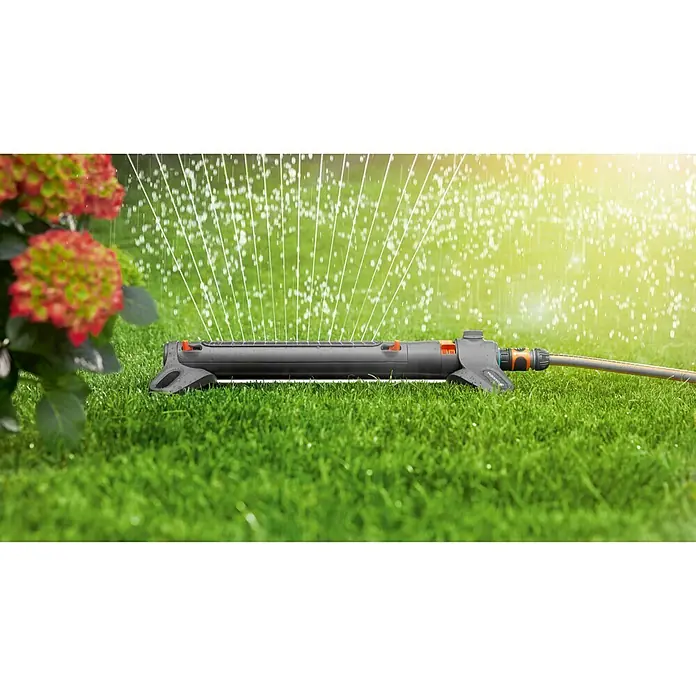 Gardena Viereckregner AquaZoom M - Max. Regnerfläche: 250 m² - Ein Gardena Vielflächenregner im Einsatz, der Rasen mit feinen Wasserstrahlen bewässert, umgeben von sattem Grün und einer blühenden Pflanze.