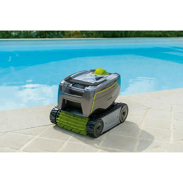 Zodiac Robot de piscina Tornax GT3220 TILE - Funcionamiento en red, Piscinas de hasta 9 x 4 m, 11 m³/h - Un robot gris de limpieza de piscinas con cepillos verdes se sienta sobre baldosas claras frente a una piscina azul.