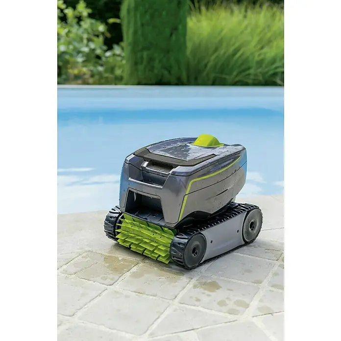 Zodiac Robot de piscina Tornax GT2120 - Funcionamiento en red, Piscinas 8 x 4 m, 11 m³/h - Primer plano de un robot de limpieza de piscinas gris y verde sentado en el borde de una piscina, con agua azul y vegetación al fondo.