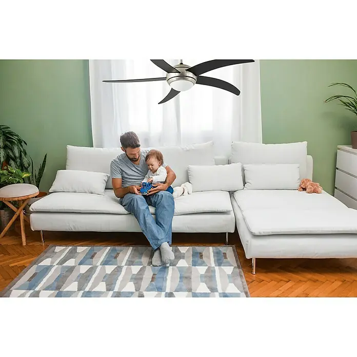 Arte confort Ventilador de techo Rocio - Negro, 132 cm, 38 W, Blanco neutro - Un padre está sentado con su hijo en un sofá debajo de un moderno ventilador de techo, proporcionando un ambiente fresco.