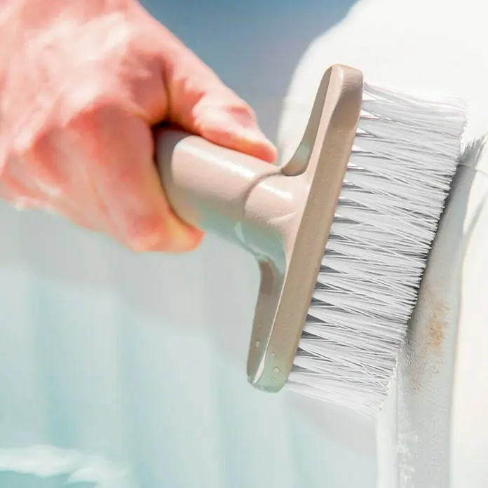 Intex Set para la limpieza de Spa - 3 pzs., Plástico, Beige - Primer plano de una mano usando un cepillo de limpieza sobre una superficie blanca.