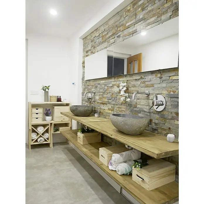 Astigarraga Caja de almacenaje - L x An x Al: 60 x 40 x 23 cm - Un baño elegante con lavabos dobles de piedra sobre estantes rústicos de madera, complementado con una pared decorativa de piedra y muebles claros.