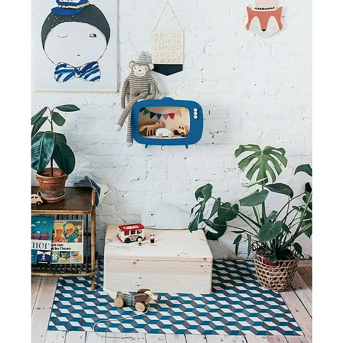 Astigarraga Caja de almacenaje - L x An x Al: 20 x 15 x 9 cm - Un cuarto infantil con un televisor de juguete azul en la pared y una caja de juguetes de madera sobre una alfombra geométrica.