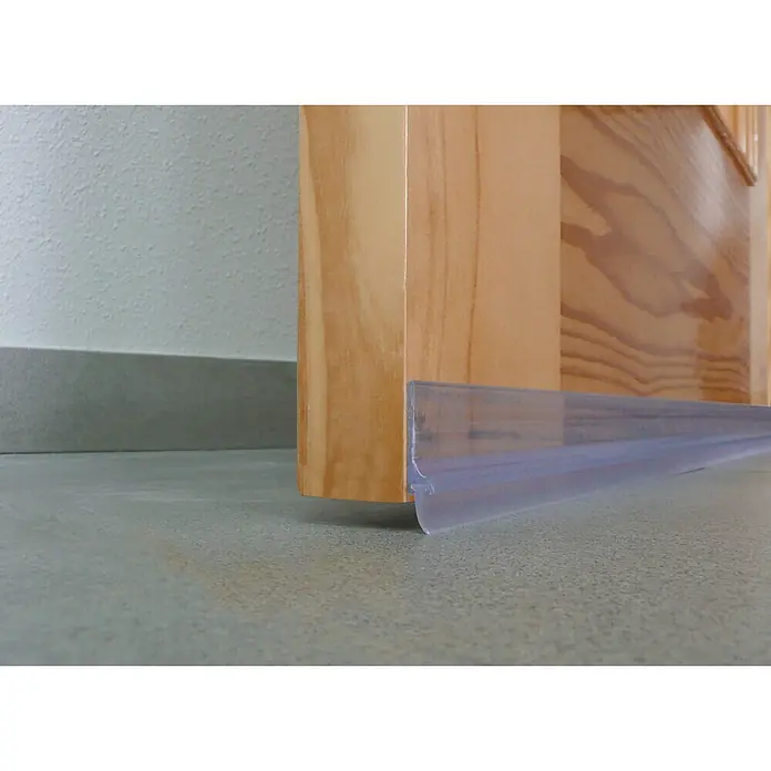Junta para puerta PVC transparente - Transparente, Largo: 1 m - Primer plano de un burlete transparente para puertas sujeto a una puerta de madera, diseñado para sellar huecos y bloquear corrientes de aire.