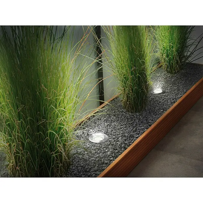Paulmann Plug & Shine Foco para empotrar en suelo - 3,6 W, Plata, Ø x Al: 9,6 x 9,2 cm - Imagen de jardín con focos empotrados entre hierbas ornamentales sobre una superficie de grava en un marco de madera.