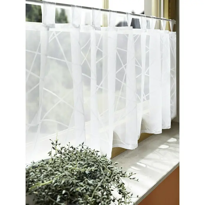 Elbersdrucke Bistrogardine Crossover - 140 x 48 cm, 100 % Polyester, Weiß - Gardine mit geometrischem Muster, aufgehängt an einer Stange, mit einer Zimmerpflanze im Vordergrund, die das Tageslicht sanft filtert.