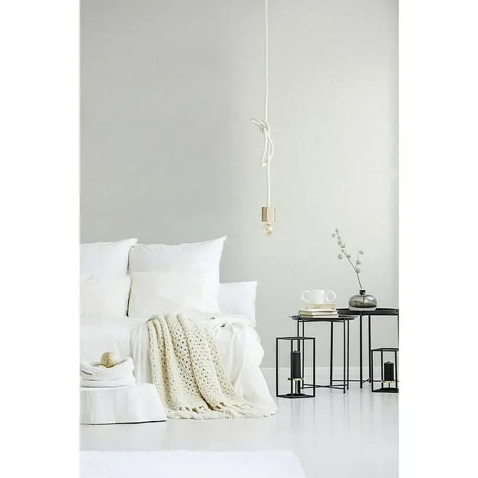 A.S. Création Geo Nordic Vliestapete - Weiß, Uni, 10,05 x 0,53 m - Minimalistisches Interieur mit einem Hängelampe mit Glühbirne, einem weißen Bett mit Kissen und einer gehäkelten Decke und schwarzen Beistelltischen.
