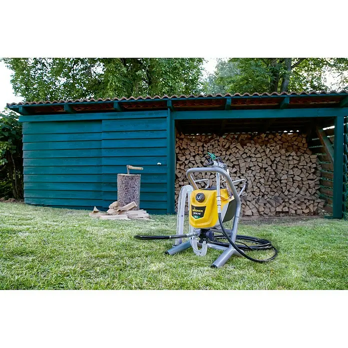Wagner High Efficiency Airless Sistema de pulverización de pintura Airless Hea 250M - 550 W, Caudal: 1,25 l/min - El Wagner Airless Sprayer amarillo frente a una caseta de madera verde. La herramienta ideal para pintar de forma rápida.