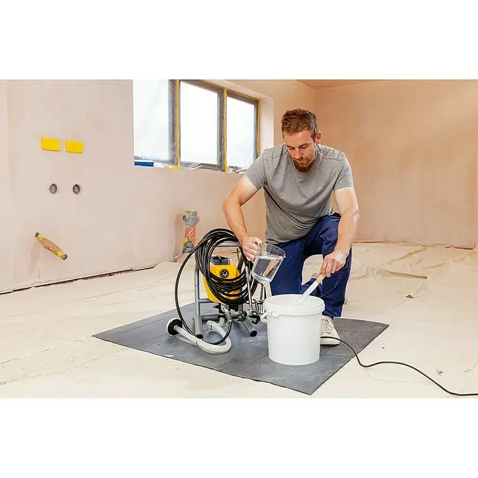 Wagner High Efficiency Airless Sistema de pulverización de pintura Airless Hea 250M - 550 W, Caudal: 1,25 l/min - Un hombre prepara un pulverizador de pintura vertiendo líquido en un cubo para diluir la pintura. El pulverizador es amarillo y negro.