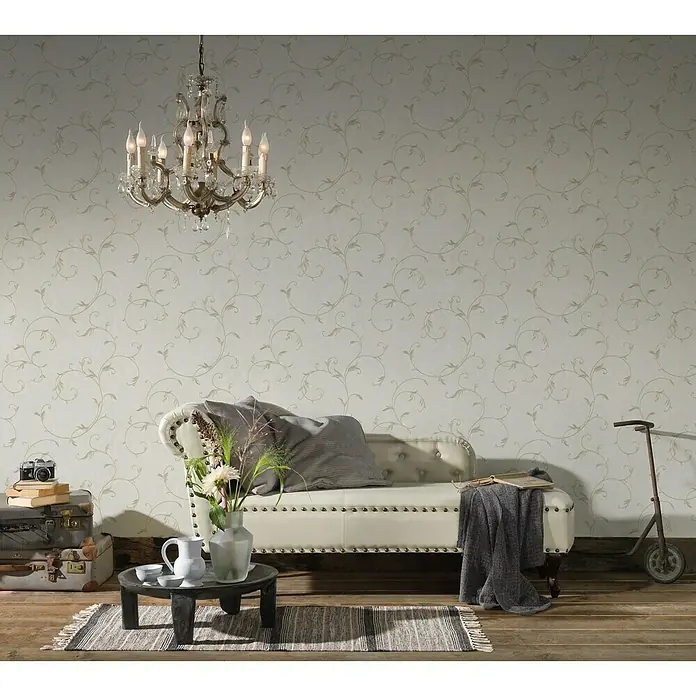 A.S. Création Romantico Vliestapete Ranke - Beige, Floral, 10,05 x 0,53 m - Ein elegantes Interieur mit einer weißen Couch, einem Tisch und einem stilvollen Kronleuchter vor einer verzierten Tapete.