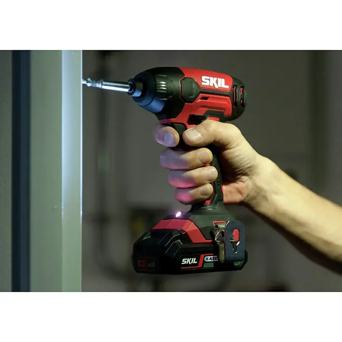 Skil PWRCore 20V Akku-Schlagschrauber 3210 CA - 20 V, Ohne Akku - Ein roter und schwarzer SKIL Akku-Schlagschrauber wird von einer Hand gehalten, während er eine Schraube in ein Objekt schraubt.