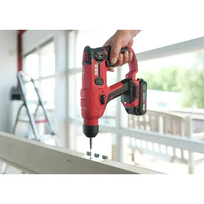 Skil PWRCore 20V Akku-Bohrhammer 3810 CA - 20 V, Ohne Akku - Nahaufnahme eines roten SKIL Akku-Bohrhammers bei der Arbeit an einem Holzstück, ideal für Bau- und Renovierungsprojekte.