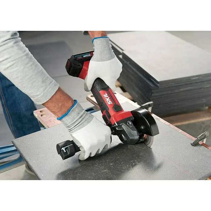 Skil PWRCore 20V Akku-Winkelschleifer 3920 CA - Ohne Akku, Durchmesser Scheibe: 115 mm - Nahaufnahme eines Akku-Winkelschleifers von Skil beim Schneiden einer Fliese, ideal für Heimwerkerprojekte.