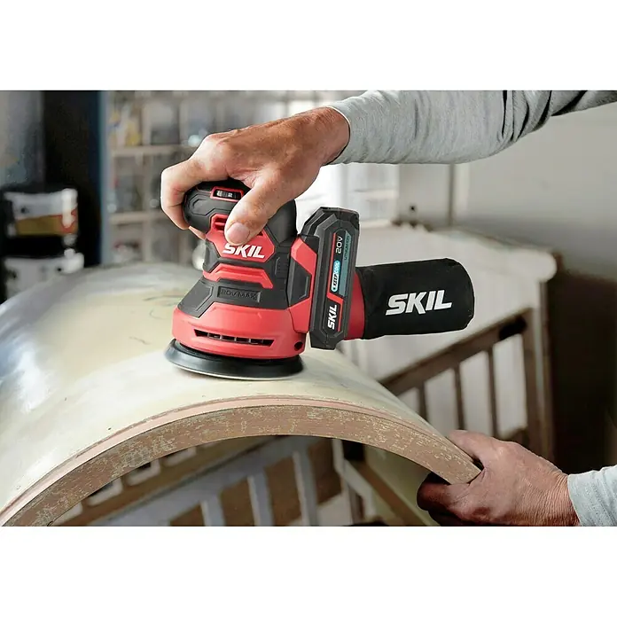 Skil PWRCore 20V Akku-Exzenterschleifer 3745 CA - 20 V, Ohne Akku, Durchmesser Schleifteller: 125 mm - Ein roter SKIL Exzenterschleifer wird zum Schleifen eines Holzes verwendet. Das Gerät verfügt über einen Staubbeutel und einen Akku.