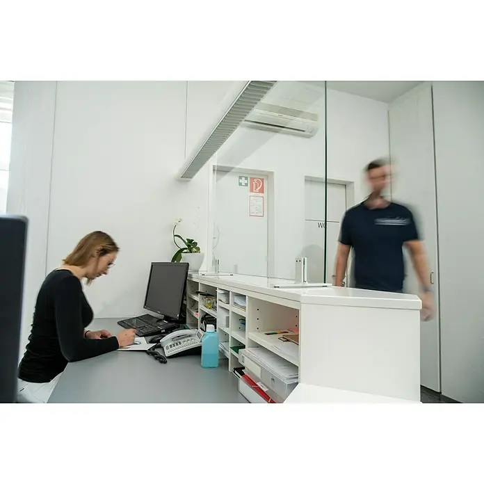 Room Plaza Hygieneschutzglas - 800 x 1.100 mm, Einscheibensicherheitsglas (ESG) - Ein transparentes Trennschutzsystem auf einem weißen Empfangstresen in einer Arztpraxis. Schützt vor Viren und Bakterien.