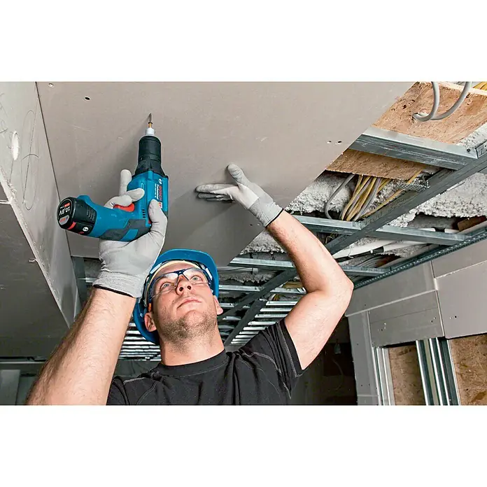 Bosch Professional Atornillador para placas de yeso de batería GTB 12V-11 LBoxx - 12 V, Sin batería, Incluye maletín - Un hombre fija un panel de techo con un taladro atornillador inalámbrico azul de Bosch. El taladro es compacto y fácil de manejar.