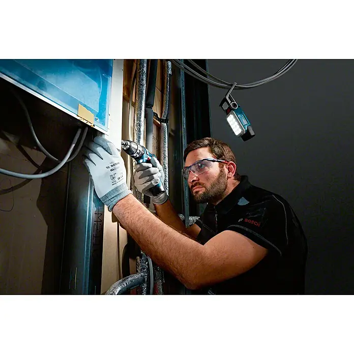 Bosch Professional Lámpara de batería GLI 12V-330 - 12 V, Sin batería, Flujo luminoso: 330 lm - Un operario utilizando un taladro Bosch y una luz de trabajo Bosch para una iluminación óptima del entorno laboral.
