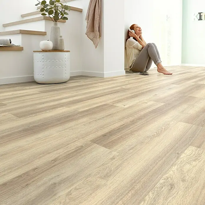 Decolife Designboden - Oak Baltic, Landhausdiele, 1.220 x 185 x 10,5 mm - Helles Laminat mit Holzmuster sorgt für eine freundliche Atmosphäre. Eine Frau sitzt an der Wand und hört Musik.