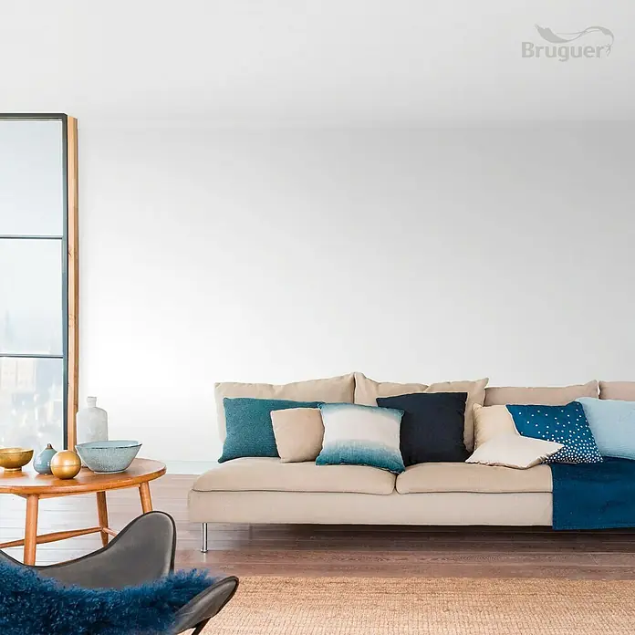Bruguer Colores del Mundo Pintura para paredes - Alaska blanco extra, Mate, 4 l - Interior moderno y luminoso con sofá beige, cojines azules y mesa de madera con cuencos decorativos. Ideal para la decoración del hogar.