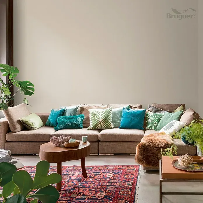 Bruguer Colores del Mundo Pintura para paredes - Alaska blanco cálido, Mate, 4 l - Acogedora sala de estar con un sofá seccional adornado con almohadas vibrantes y una mesa de centro rústica, creando un ambiente acogedor.