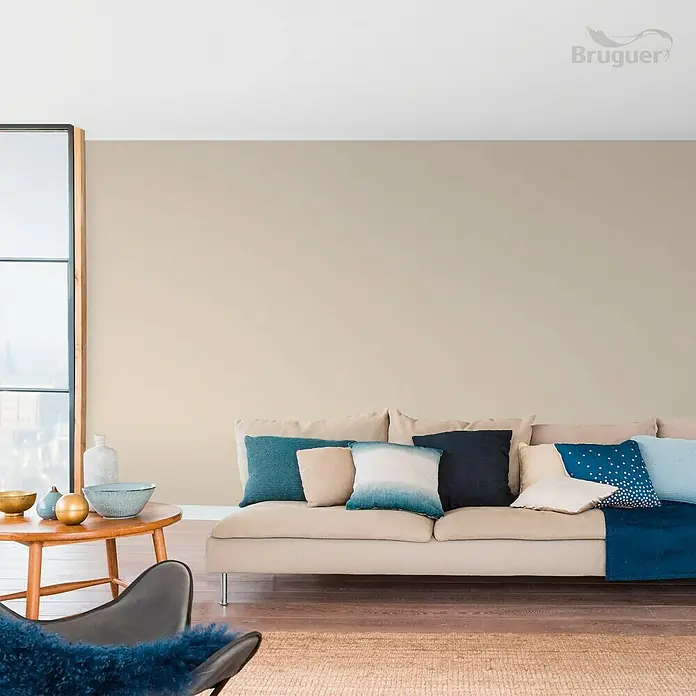 Bruguer Colores del Mundo Pintura para paredes - Alaska blanco cálido, Mate, 4 l - Pintura de pared clara de Bruguer en un salón acogedor con sofá, cojines y mesa de madera para un ambiente cálido y acogedor.