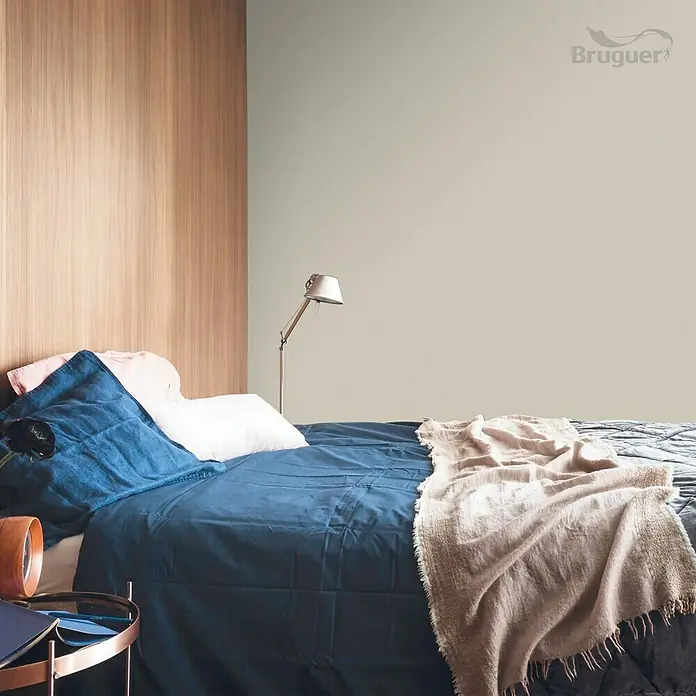 Bruguer Colores del Mundo Pintura para paredes - Alaska blanco cálido, Mate, 4 l - Elegante dormitorio con ropa de cama azul y una cálida manta beige, iluminada por una lámpara moderna. Paneles de madera y pintura Bruguer al fondo.