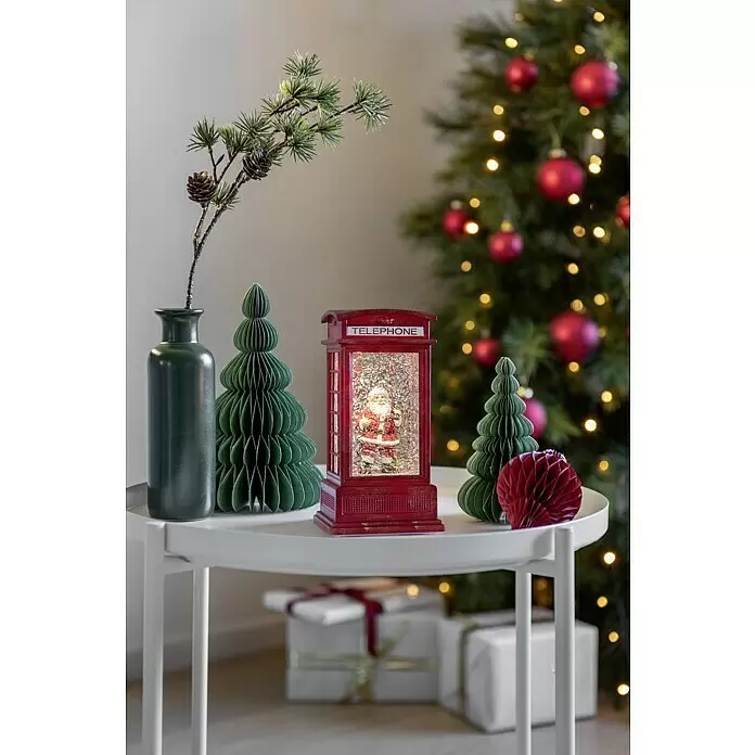 Konstsmide LED-Schneelaterne - Innen, Rot, 9,5 x 9,5 x 20 cm, Laterne, Batteriebetrieben - Weihnachtsdekoration: eine rote Telefonzellen-Schneekugel mit Weihnachtsmann, grüne Papierbäume und ein Tannenzweig in einer Vase.