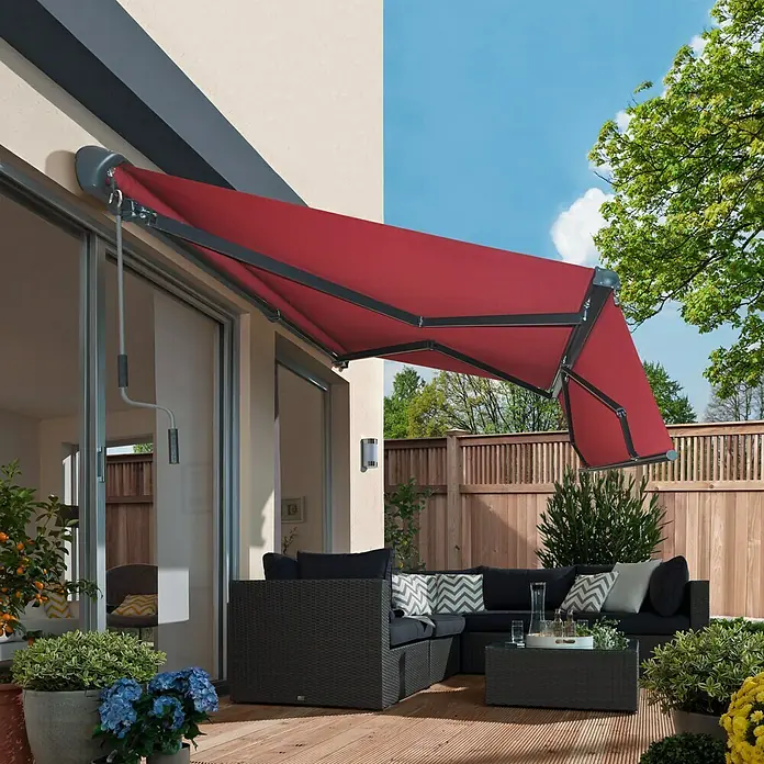 Sunfun Gelenkarmmarkise - Bordeaux, Breite: 3,95 m, Ausfall: 3 m - Nahaufnahme einer roten Markise, die an einem modernen Haus angebracht ist und Schatten auf eine stilvolle Terrasse mit Gartenmöbeln spendet.