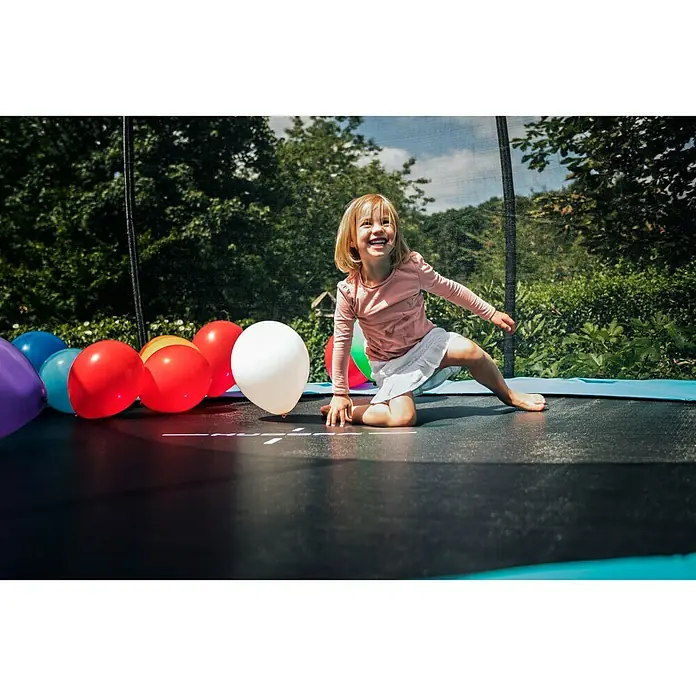 Hudora Trampolin Fantastic Complete 300 V - Durchmesser: 300 cm - Ein fröhliches Mädchen spielt auf einem Trampolin mit bunten Ballons im Garten. Das Trampolin bietet sicheren Spaß für Kinder im Freien.