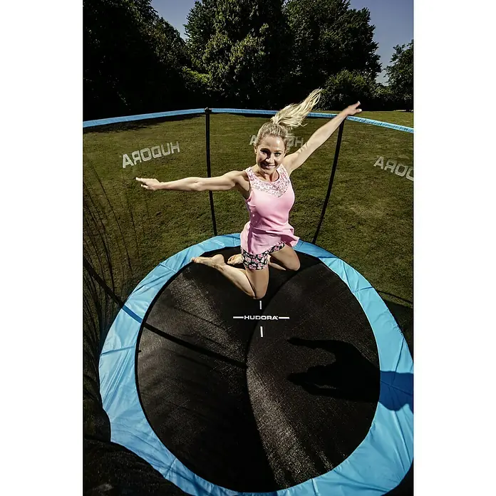 Hudora Trampolin Fantastic Complete 300 V - Durchmesser: 300 cm - Ein sonniges Bild zeigt eine Frau auf einem HUDORA-Trampolin, die mit ausgestreckten Armen springt, während sie sich im Freien vergnügt.