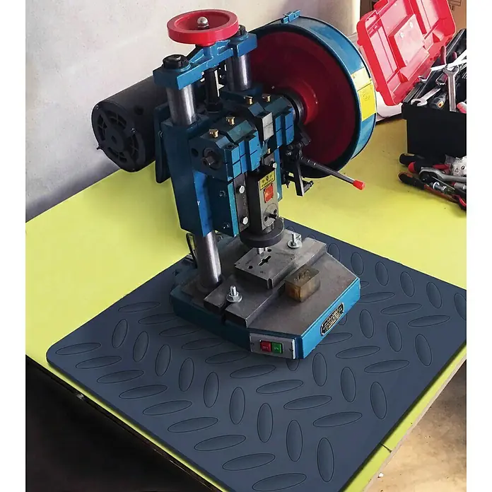 Estera antideslizante - L x An: 60 x 60 cm, Negro - Primer plano de una remachadora azul sobre una mesa amarilla, utilizada para el remachado profesional de diversos materiales.