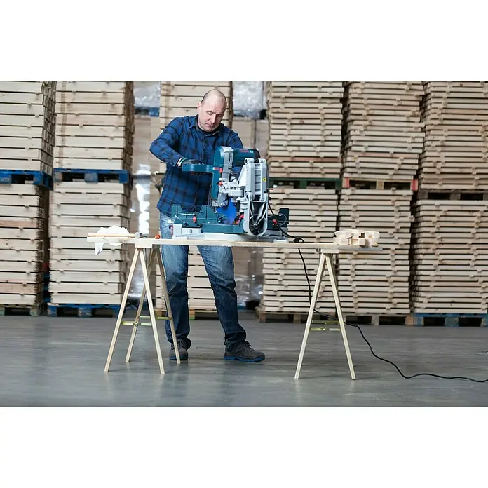 Astigarraga Holzklappbock Kipli - Tragkraft: 250 kg, Höhe: 73,5 cm, Kiefer - Ein Mann benutzt eine Bosch Kapp- und Gehrungssäge auf einer Werkbank in einer Lagerhalle, um Holz zu sägen.