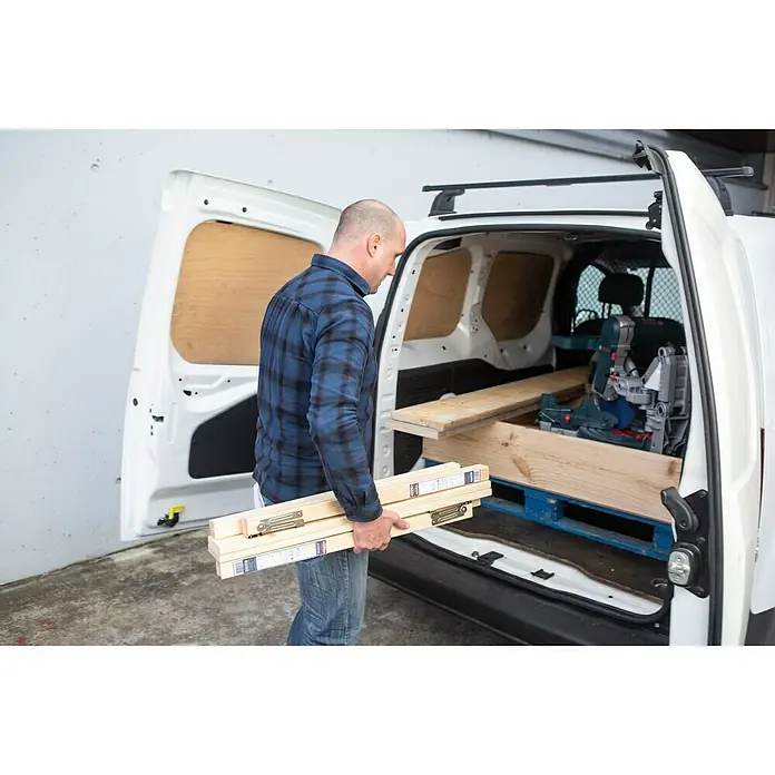 Astigarraga Holzklappbock Kipli - Tragkraft: 250 kg, Höhe: 73,5 cm, Kiefer - Ein Mann trägt Holzlatten zu einem Lieferwagen, in dem sich bereits Baumaterialien und Werkzeuge befinden.