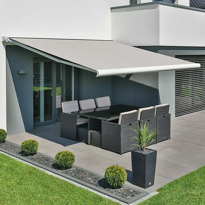 Deyo Limassol Vollkassettenmarkise - Beige Struktur, Farbe Gestell: Signalweiß, Breite: 3,5 m, Ausfall: 3 m - Eine moderne Terrassenüberdachung bietet Schatten über einem eleganten Esstisch mit Rattansesseln und üppigem Grün.
