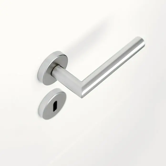 Diamond Doors Modern Zimmertürgarnitur L-Form BB - Stärke Tür: 38 mm - 45 mm, Edelstahl, Buntbart - Nahaufnahme einer modernen, silbernen Türklinke mit Schlüsselloch auf einer weißen Tür. Das Design ist minimalistisch und elegant.