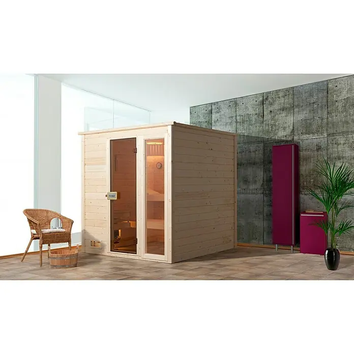 Finnwood Massivholzsauna Bjoern Trend 1 - Bioofen, Steuerung Ofen: Extern, L x B x H: 148 x 198 x 203 cm - Diese Aufnahme zeigt eine freistehende Sauna aus hellem Holz mit Glastüren, ergänzt durch einen Korbstuhl und eine Zimmerpflanze.