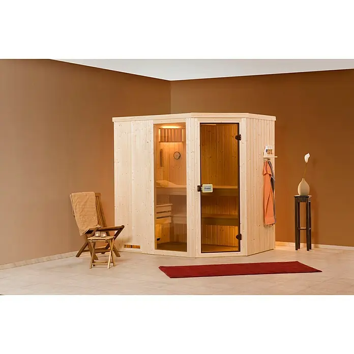 Finnwood Elementsauna Ronja Trend 3 - Elektroofen, Steuerung Ofen: Extern, L x B x H: 194 x 194 x 199 cm - Eine moderne Ecksauna aus hellem Holz mit Glastüren. Bequemer Stuhl und Hocker davor, ein roter Teppich auf dem Boden.