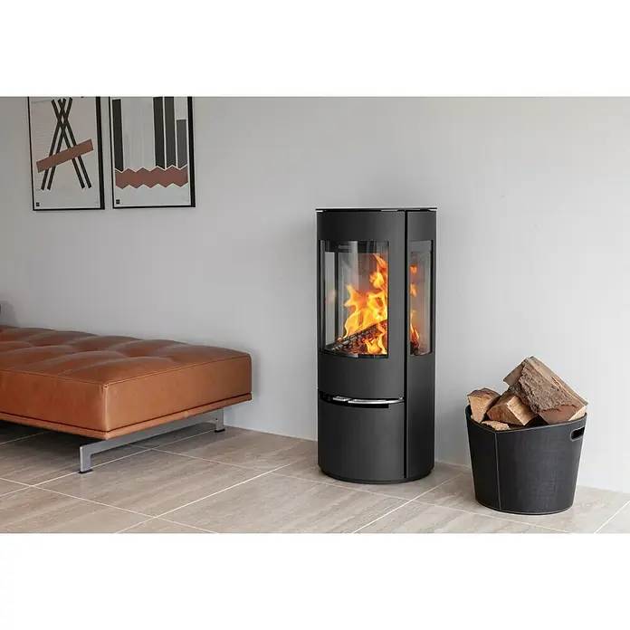 Aduro Kaminofen 22 - 5,5 kW, Raumheizvermögen: 340 m³, Material Verkleidung: Stahl, Schwarz - Ein moderner Kaminofen mit Glasfenster, in dem ein gemütliches Feuer brennt, daneben ein Korb mit Holzscheiten in einem stilvollen Wohnraum.