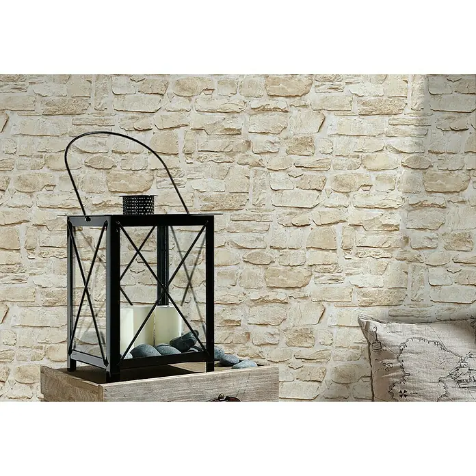 A.S. Création Il Decoro Vliestapete Steine - Beige, Steinoptik, 10,05 x 0,53 m - Dekorative Laterne mit Kerzen und Steinen, platziert auf einer Holzkiste vor einer Steinwand, die eine warme, gemütliche Atmosphäre schafft.