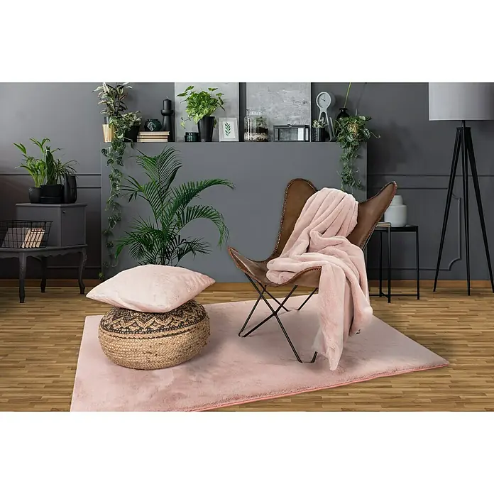 Kissen HappyPuderrosa, 48 x 48 cm, 100 % Polyester - Detailaufnahme eines Interieurs mit einem rosa Teppich, einem Ledersessel und üppigen Pflanzen, die ein gemütliches und stilvolles Ambiente schaffen.