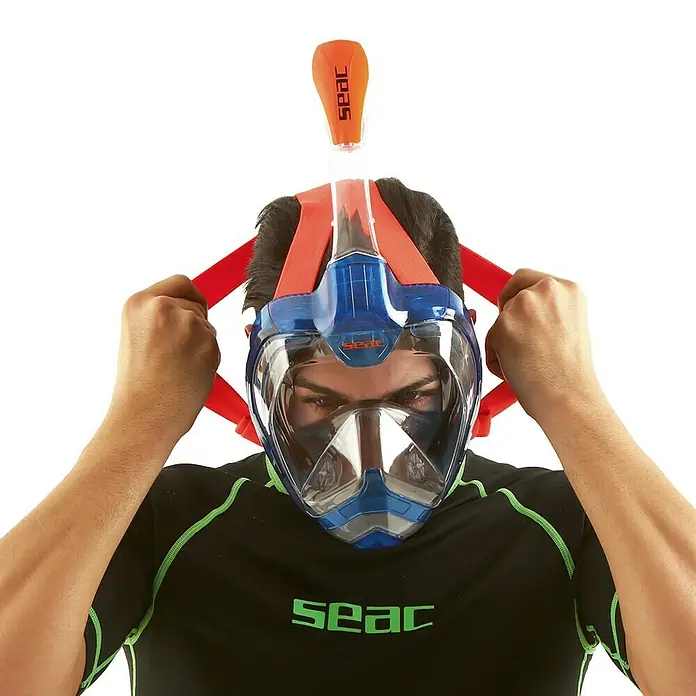 Seac Sub Máscara de Snorkel Mágica - S/M, Plástico, Azul/Naranja - Hombre poniéndose una máscara de snorkel facial completa SEAC azul con correas naranjas, con snorkel desmontable.