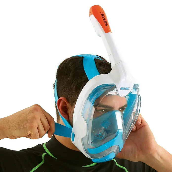 Seac Sub Máscara de Snorkel Mágica - S/M, Plástico, Azul/Blanco - Un hombre se ajusta una máscara de snorkel facial completa SEAC. La máscara es blanca y azul con un tubo de respiración naranja.
