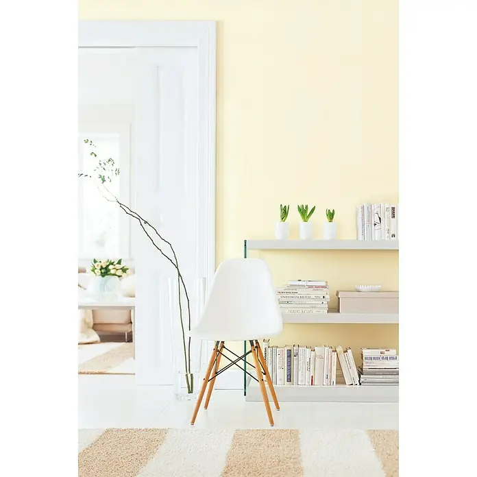 SCHÖNER WOHNEN-Farbe MyColour Wandfarbe - My Ivory, Matt, 10 l - Helles Interieur mit einem weißen Stuhl mit Holzbeinen vor einem Regal voller Bücher und grünen Pflanzen.