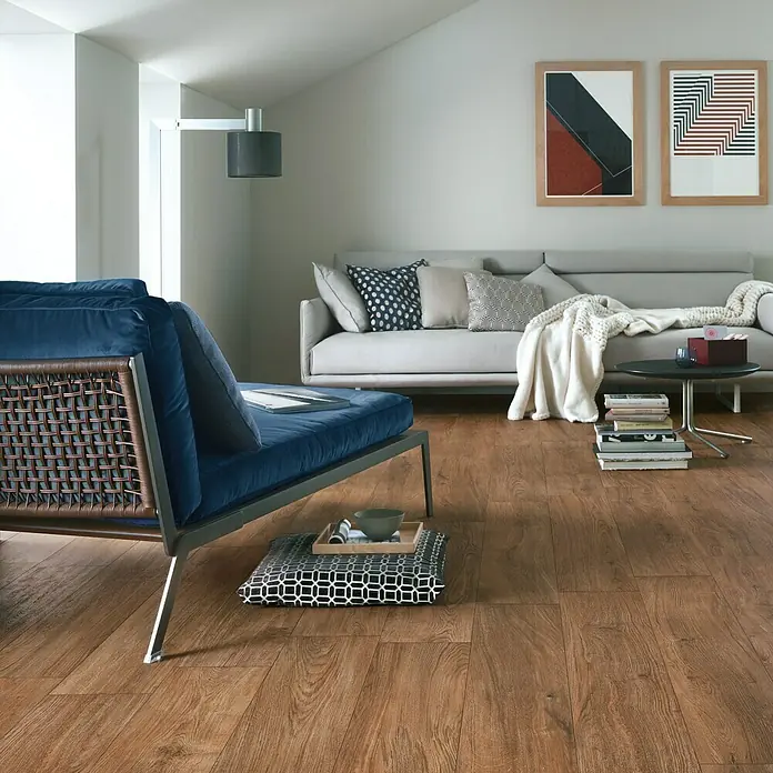 Harmonie by Palazzo Feinsteinzeugfliese - 30 x 120 cm, Eiche Dunkel, Matt - Holzboden im Wohnzimmer mit blauen Polstermöbeln, Couch und Tisch. Attraktives, gemütliches Design mit warmem Farbton.