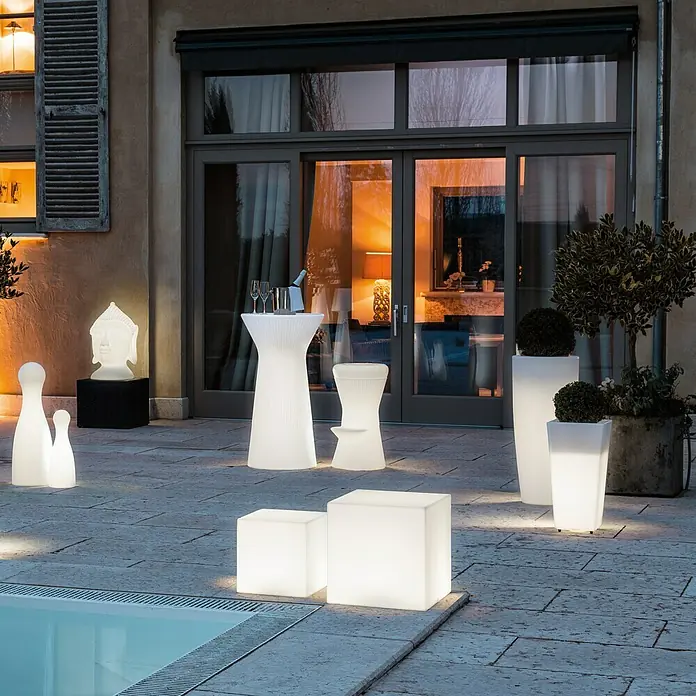 New Garden Design-Außenleuchte Cuby 3232 x 32 x 32 cm, Warmweiß - Elegante Außenansicht mit beleuchteten Gartenmöbeln, darunter würfelförmige Sitze, Säulen und Buddha-Kopf.