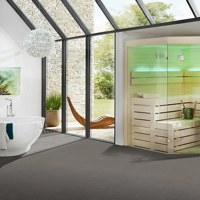 Vinylbodenmuster Strong SPC Travertin Maragha - 280 x 160 x 3,8 mm, Steinoptik - Ein modernes Badezimmer mit einer freistehenden Badewanne, einer Sauna mit Glasfront und einem stilvollen Holzsessel im Hintergrund.